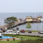 Entry area of Municipal Pier Rose Garden in Fairhope, Alabama, with a bridge, fountain, and mature oak trees in the background.