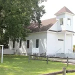 The historic white chapel at Semmes Heritage Park under the shade of a massive Oak tree in Alabama.